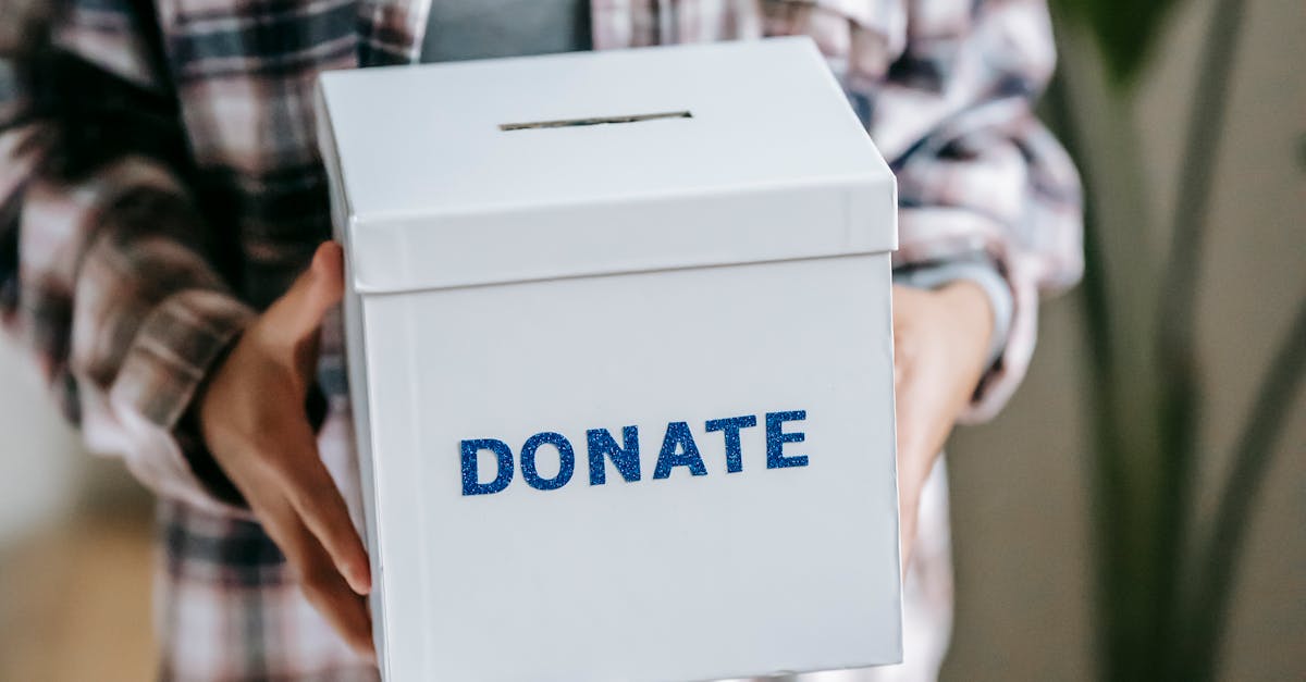 Crop unrecognizable woman in casual clothes standing with box for donations in hands on light room